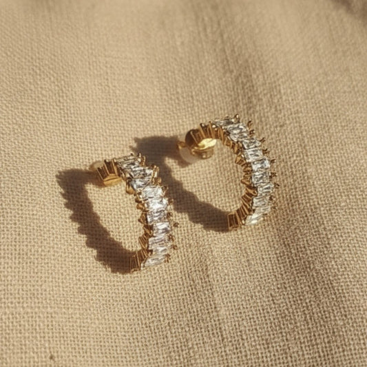 Scintilla Zirkonia Creolen in Gold auf hellem Leinenstoff mit warmem Licht und Schatten.
