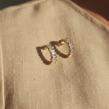 Scintilla Creolen aus Edelstahl mit Zirkonia-Steinen auf beigem Leinenstoff.