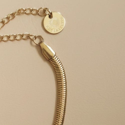 Detailaufnahme des goldfarbenen Serena Snake Armbands mit Karabiner, Verlängerungskette und EDELATELIER.-Logoplättchen.