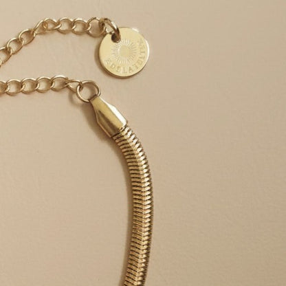 Detailaufnahme des goldfarbenen Serena Snake Armbands mit Karabiner, Verlängerungskette und EDELATELIER.-Logoplättchen.