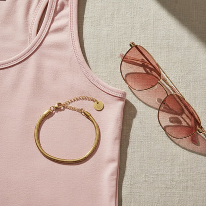 Goldfarbenes Serena Snake Armband auf rosa Oberteil neben Sonnenbrille im sommerlichen Look.