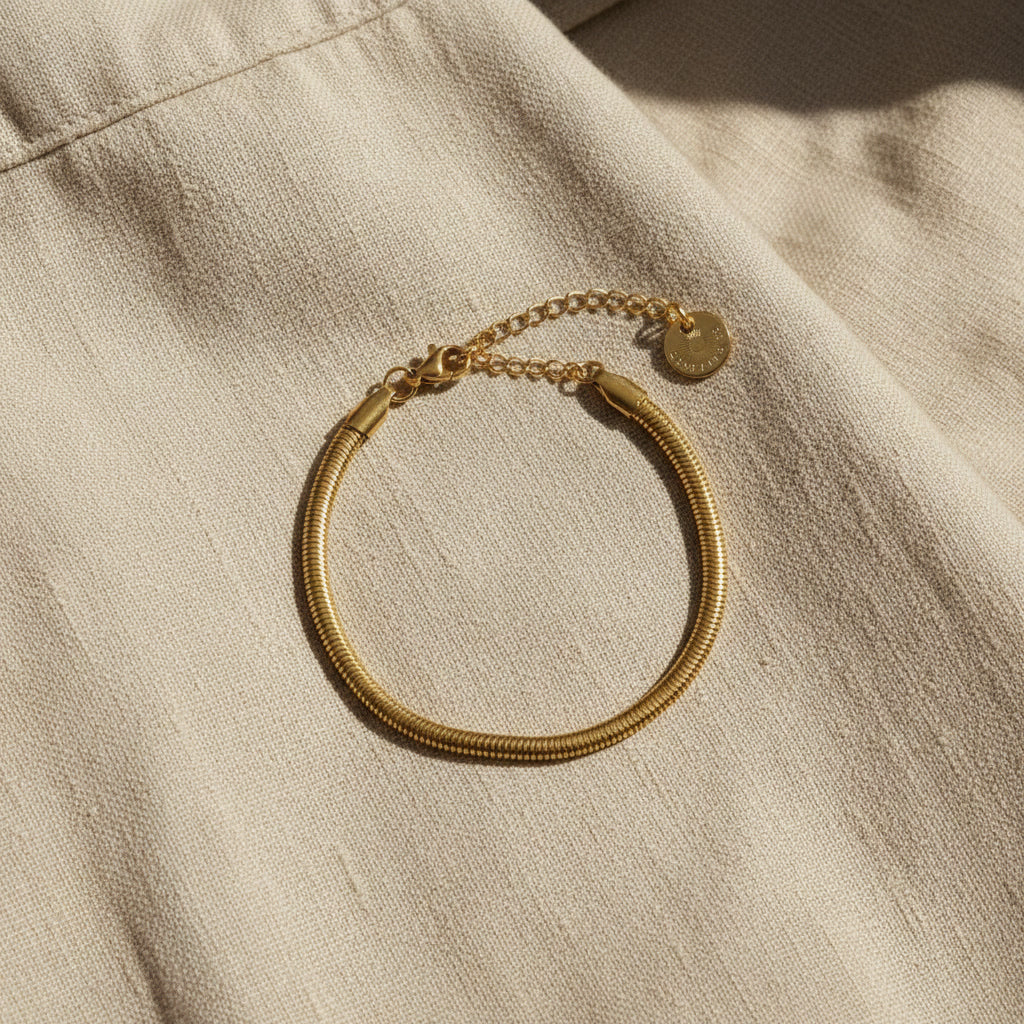 Goldfarbenes Serena Snake Armband auf beigem Leinenstoff im warmen Sonnenlicht.