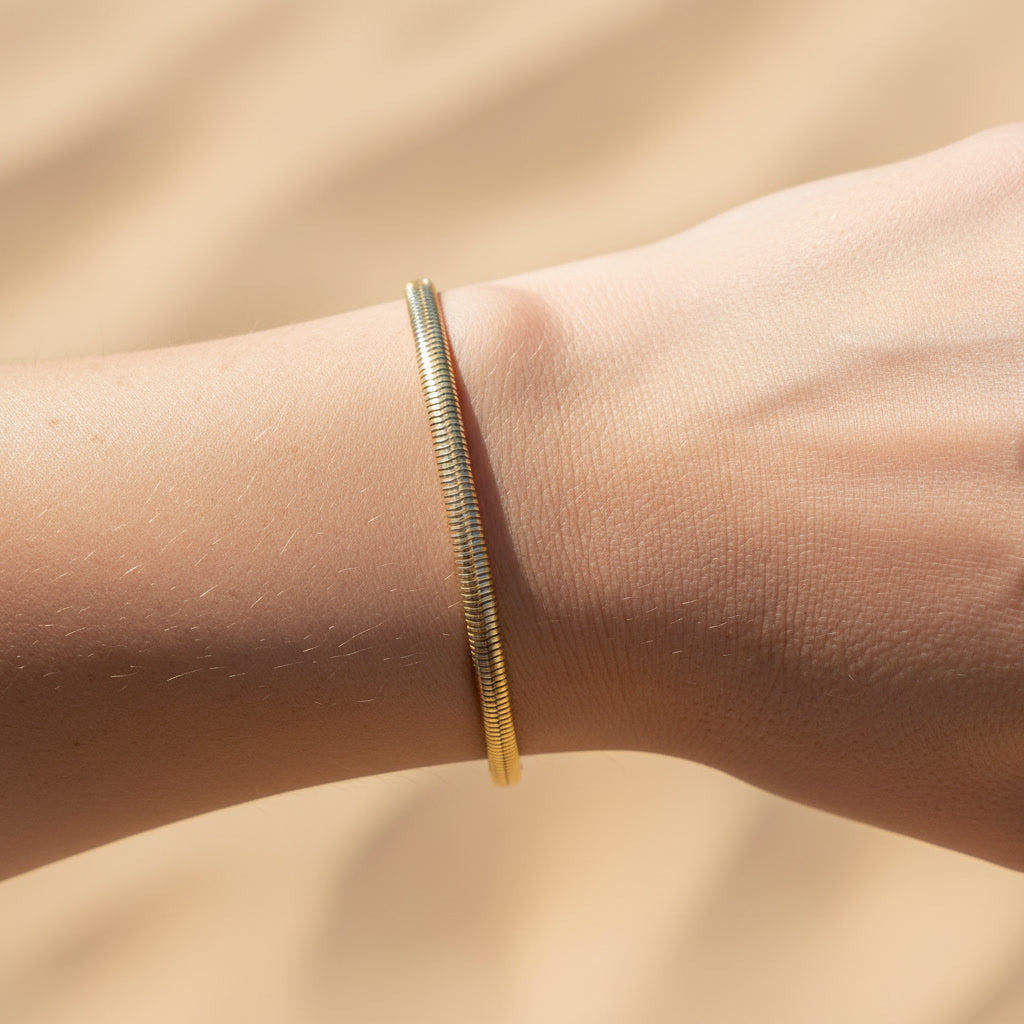 Goldfarbenes Serena Snake Armband mit flacher Snake-Struktur, getragen am Handgelenk im warmen Sonnenlicht.