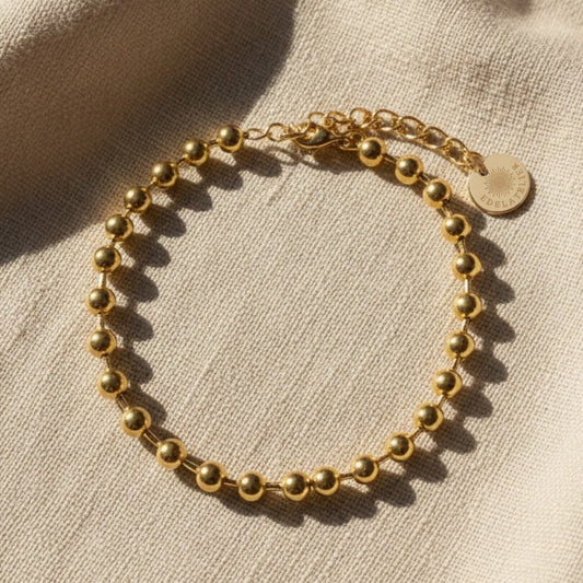Sfera Armband aus vergoldetem Edelstahl 304L mit 5 mm Kugeln und Verlängerungskette auf beigem Hintergrund.