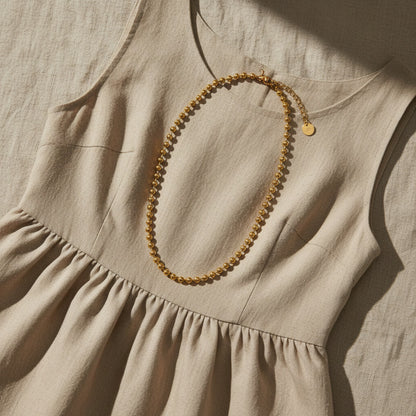 Goldfarbene Sfera Halskette auf beigem Leinenkleid.