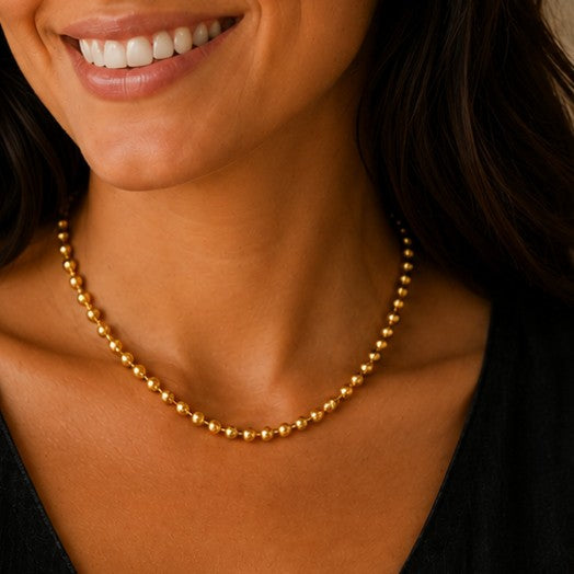 Model trägt goldfarbene Sfera Halskette mit Kugelstruktur zu schwarzem Leinenkleid.