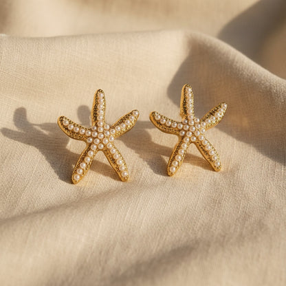 Stella Marina Ohrringe in Gold mit weißen Perlen auf hellem Leinen