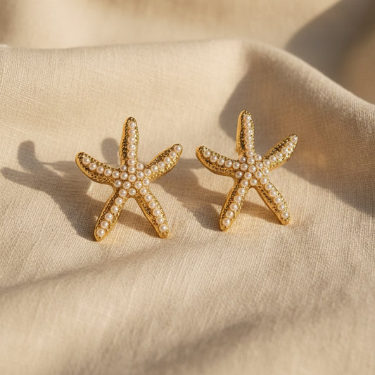 Stella Marina Ohrringe in Gold mit weißen Perlen auf hellem Leinen
