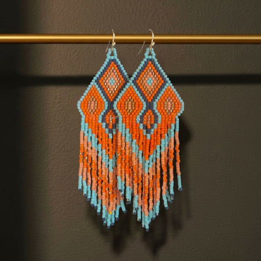 Handgewebte lange Statement-Ohrringe Terra e Mare von EDELATELIER. in erdigem Terrakotta, Orange und Türkis, elegant hängend an einer goldenen Stange vor hellem Hintergrund.