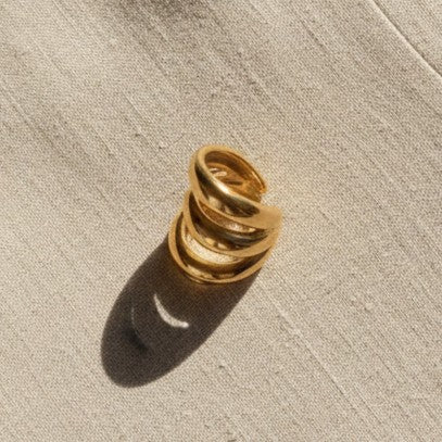 Goldener Ear Cuff mit dreifacher Ringform auf hellem Leinenstoff