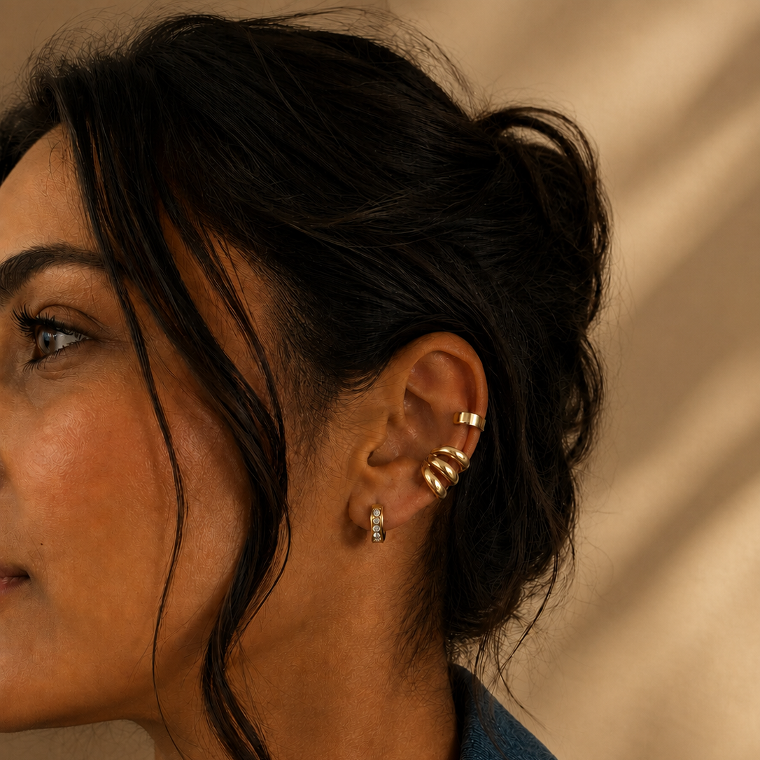 Treccia Ear Cuff in Gold am Ohr getragen, kombiniert mit kleinem Creolenstecker.