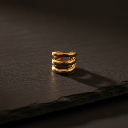 Goldener Treccia Ear Cuff aus Edelstahl mit dreifacher Ringform auf dunklem Hintergrund.