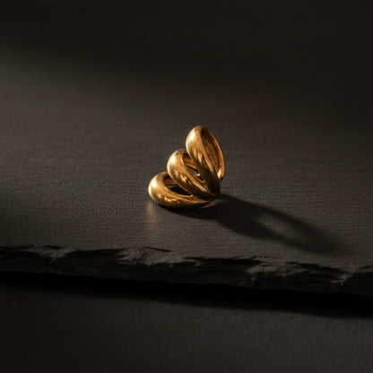 Goldener Ear Cuff ohne Ohrloch mit geschwungener dreifacher Form auf schwarzem Hintergrund.