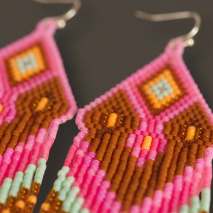 Extreme Makro-Nahaufnahme der handgewebten Miyuki-Perlen von EDELATELIER., die die präzise Anordnung der altrosafarbenen und goldenen Perlen im Detail des Modells Tropica Rosa zeigt.