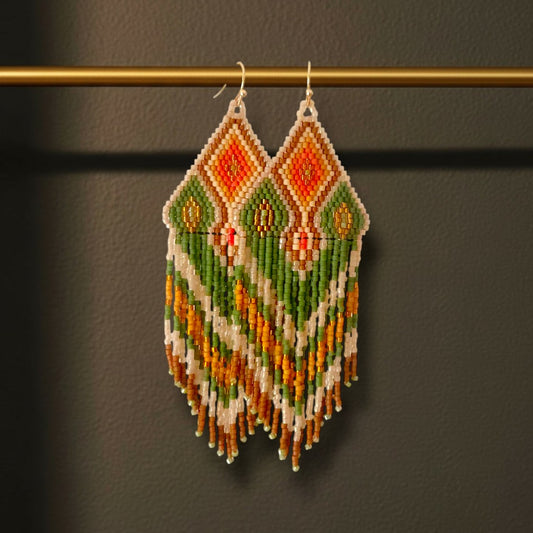 Ein Paar handgefertigte Statement-Ohrringe Modell Verde Tropicale von EDELATELIER, präsentiert an einer goldenen Stange. Die 10 cm langen Ohrringe zeigen ein lebendiges, tropisches Muster in sattem Grün und leuchtendem Orange, kombiniert mit cremeweißen Akzenten und feinen Golddetails.