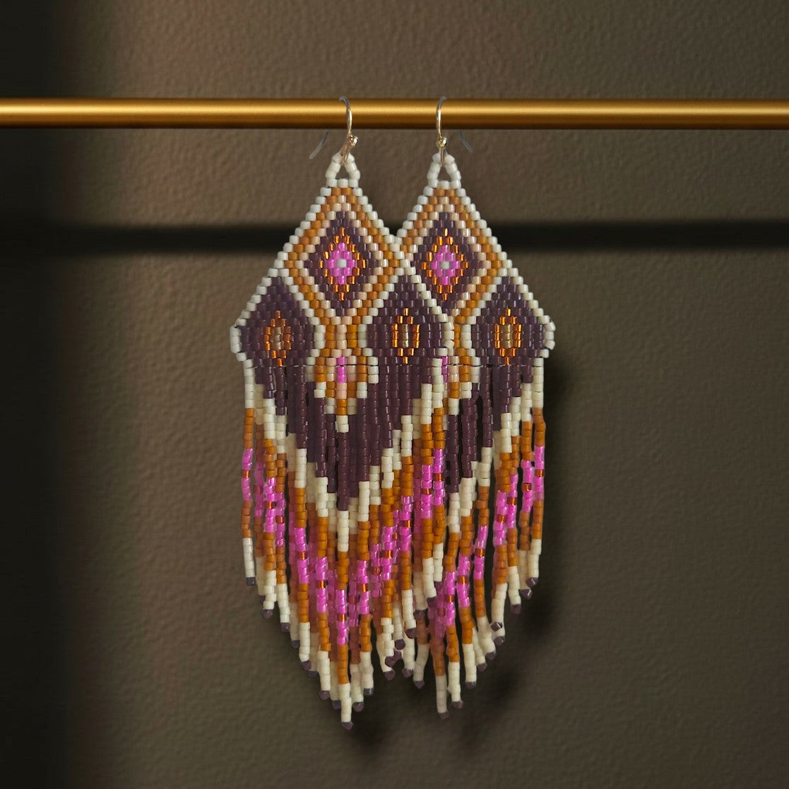 Ein Paar handgefertigte Statement-Ohrringe Modell Wine Aurora von EDELATELIER, präsentiert an einer goldenen Stange. Die 10 cm langen Ohrringe zeigen ein elegantes Muster in tiefem Weinrot und dunklem Violett, kombiniert mit leuchtendem Pink, Creme und herbstlichen Brauntönen.